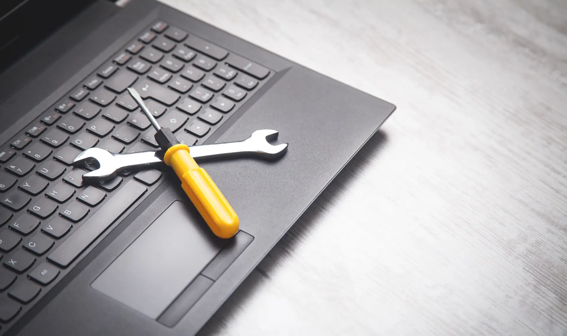 Naslovna Wrench and screwdriver on laptop keyboard — concept of IT support, computer repair, and technical maintenance services.